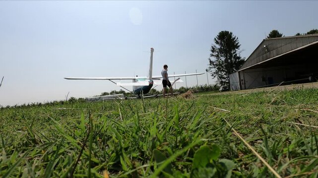 An athletic looking woman walks around a small aircraft, a Cessna 182, and examines it