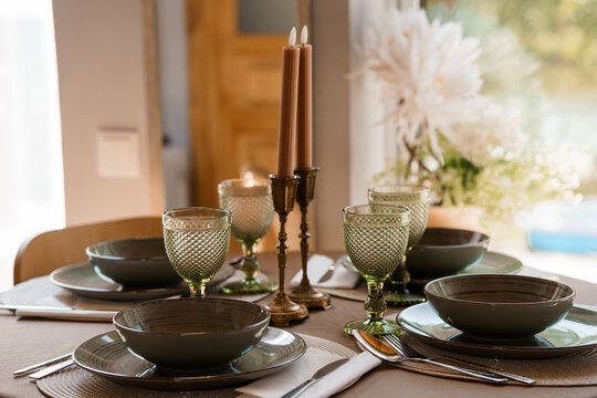 Elegant Autumnal Table Setting with Green Glassware, Grey Plates, and Candles. Cozy Dining Scene with Natural Light and Decorative Elements.