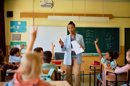 African American elementary school teacher pointing at student with raised arm who wants to answer question.
