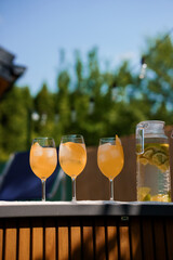 Summer Refreshments: Three Glasses of Aperol Spritz on Deck with Lemon Infused Water Pitcher and...