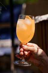 Hand Holding Orange Aperol Spritz in Glass Outdoors, Summer Drink, Sunny Patio, Blue Striped...
