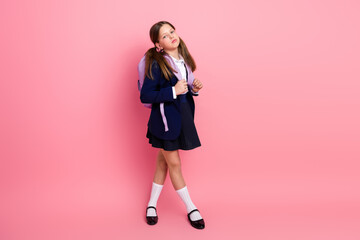 Charming young schoolgirl posing with backpack against pink background in stylish uniform during back to school season