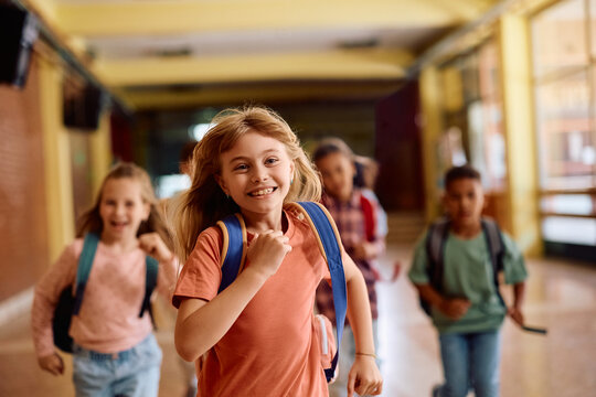 Happy girl and her classmates having fun while running through hallway at school.