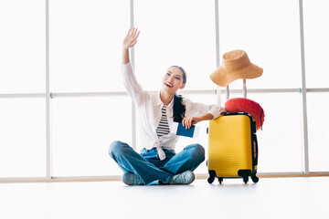 Young female traveler at the airport sitting with luggage ready for her vacation adventure, holding...