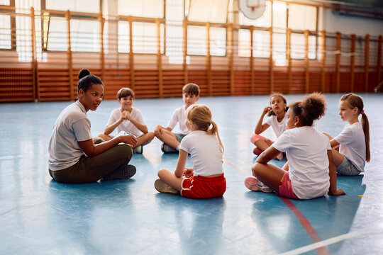 Fototapeta Black physical education teacher communicating with her students at school gym.