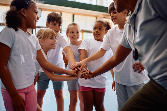 Happy kids and their coach joining hands in unity during PE class at school.