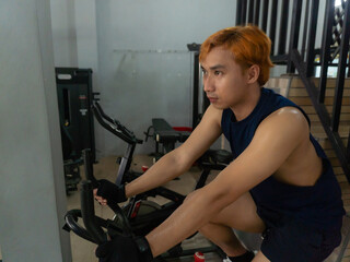 young sports indonesia asian man in blue cycling in fitness center. Cardio workout, leg workout,...
