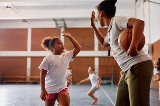Happy black schoolgirl and her sports teacher giving high-five during PE class. - Powered by Adobe