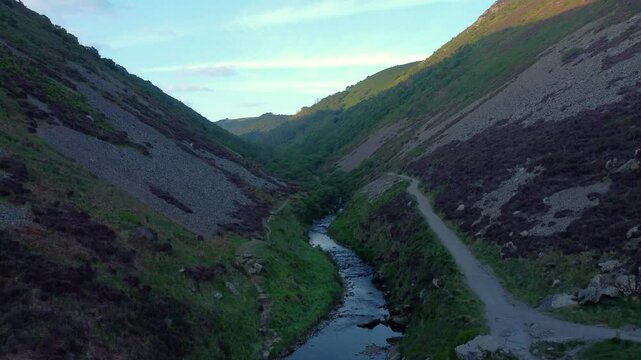 Fast Rising Drone View of Deep Valley Covered in Shadow as Sunrise Sun Enters on Far Side with Bright Blue Sky with Scattered Clouds.