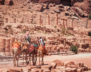 locals riding camels through the ancient ruins of Petra, Jordan, surrounded by historic stone columns and sandstone structures