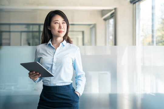 Dreaming thoughtful portrait of mature Asian woman business specialist female manager. Professional businesswoman CEO holding digital tablet using fintech tab for work in modern office. Copy space