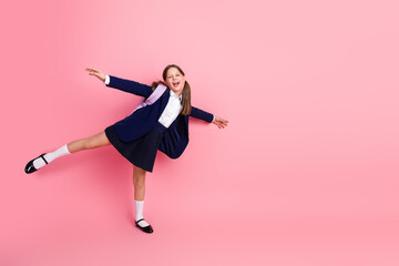 Happy schoolgirl in uniform with ponytails joyfully posing on a vibrant pink background...