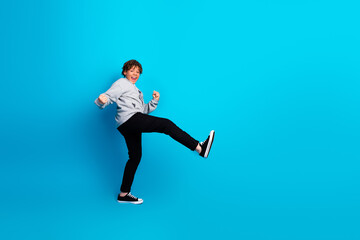 Cheerful boy showcasing energetic dance moves against blue background wearing casual attire...
