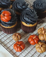 A collection of spooky  delicious Halloween-themed cupcakes with rich, dark black swirled frosting and with charming edible pumpkin decorations in various shades of orange and natural pumpkin tones.