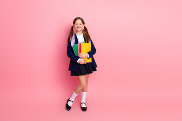Fototapeta na wymiar Portrait of a cheerful schoolgirl in uniform holding colorful notebooks against a pink background, symbolizing education and learning