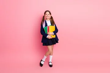 Fototapete Rund Portrait of a cheerful schoolgirl in uniform holding colorful notebooks against a pink background, symbolizing education and learning © deagreez