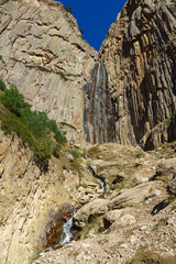 Beautiful Abai-Su waterfall cascades down rugged cliffside, surrounded by lush greenery and rocky terrain, creating picturesque natural scene. Kabardino-Balkaria, Chegemsky district