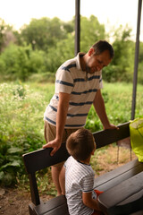 father and son are relaxing outdoors under a canopy. recreation area. son is playing around, having...
