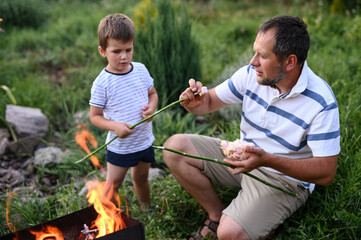Dad and son roasting marshmallows on barbecue in  garden backyard, bonding over campfire, outdoor...