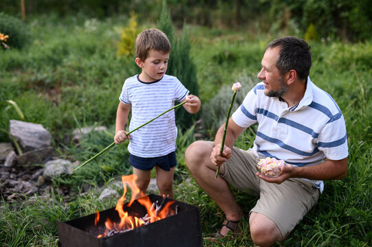 Dad and son roasting marshmallows on barbecue in garden backyard, bonding over campfire, outdoor family time, parenting, slow living, childhood memories, quality time together