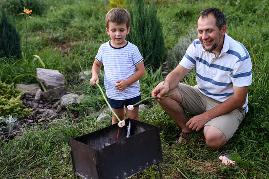 Dad and son roasting marshmallows on barbecue in garden backyard, bonding over campfire, outdoor family time, parenting, slow living, childhood memories, quality time together