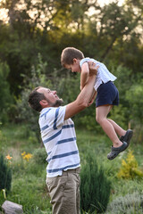 Happy father and  son playing outside in garden in summer in sun. dad roll son on neck, roll on...