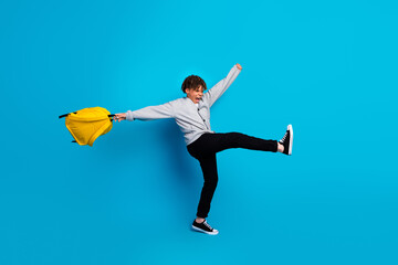 Energetic student with yellow backpack demonstrating happiness and enthusiasm on blue background,...