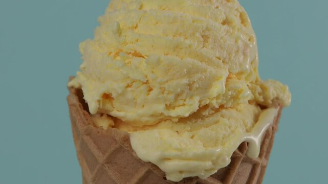 close up of yellow gelato scoop in waffer coner blue background zoom