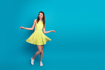 Attractive young woman in a yellow summer dress posing against a blue background exuding charm and...