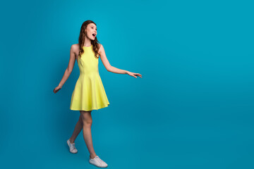 Young fashionable woman in a stylish yellow dress posing with confident expression against a bright blue background
