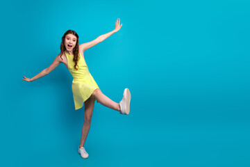 Delightful young woman in a vibrant yellow dress posing on a bright blue background celebrating...