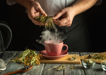 A person skillfully prepares herbal tea by steeping fresh herbs in a pink cup. Steam rises from the...