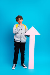 Smiling schoolboy posing with a pink arrow on a vibrant blue vertical background, expressing...