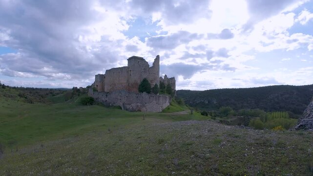 Medieval stone walls rising over green valley under cloudy sky