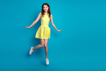 Young woman in a stylish yellow dress joyfully posing against a vibrant blue background with a...