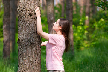 Young woman leaning against a tree in the forest enjoying a moment of oneness with nature
