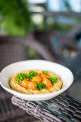 Close-up of creamy pasta with orange sauce and parsley in a white bowl on a wicker table, served outdoors in natural light