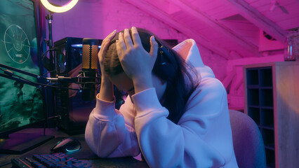 Frustrated sad woman gamer girl female streamer in headphones worry upset with fail loss bad result failure at computer online game playing in neon home room at night addiction gaming problem stream © Yuliia