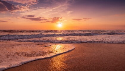 Obraz premium sunset over ocean waves rolling onto sandy beach with warm orange and pink sky hues