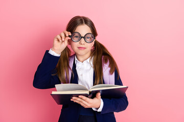 Young schoolgirl with glasses reading and posing for a fun educational photoshoot on a playful pink...