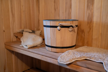 Wooden sauna interior with bucket, mittens, and towel on wooden shelf