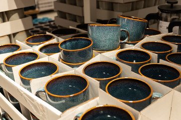 Display of blue ceramic mugs with orange rims in cardboard boxes at a retail store