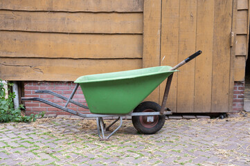 Green wheelbarrow against wooden wall in rustic outdoor setting