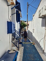 Sunlit Mediterranean street with blue accents and single pedestrian evoking summer lifestyle, cultural charm, and architecture for travel and leisure visuals