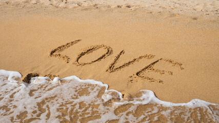Love written on sandy beach with ocean waves approaching