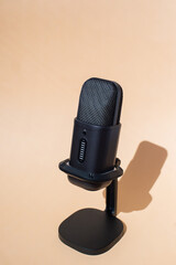Black studio microphone on stand with beige background in natural light