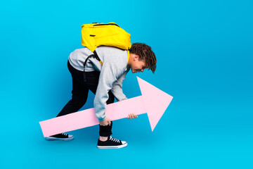 Young student holding pink arrow sign wearing backpack, expressing education themes on vibrant blue...