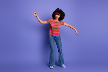 Young woman with curly black hair in a casual striped t-shirt striking a playful pose against a...