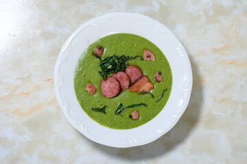 Delicious homemade green soup with sausage and cabbage in a white dish