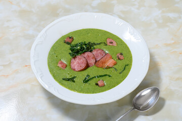 Delicious green soup with sausage, cabbage and bancon on a white plate